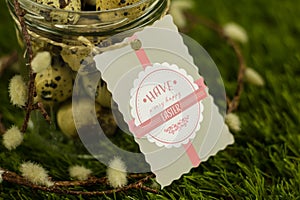 Jar filled with quail eggs and a happy easter badge on grass