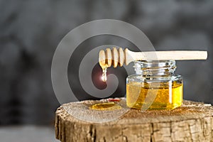 Jar with fresh bee honey and wooden dipper on a gray background. Space for text