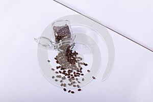 A jar of fresh fragrant coffee beans, on a white background. Hard shadow from the sun, art concept of morning and energy charge