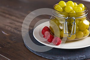 Jar of fresh grapes, blueberries and raspberries on white plate and slate plate in overhead view