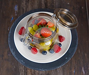 Jar of fresh grapes, blueberries and raspberries on white plate and slate plate in overhead view