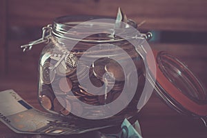 Jar full of coins of euro with a bills on the table - earining money to travel the world and go to vacations alone or with friends