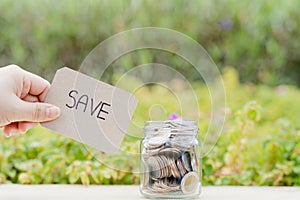Jar full of coins with save word paper on blurred green natural background. Saving money and investment concept