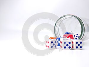 a jar full of dice with some colored ones scattered around it