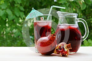 A jar and glass of pomegranate juice with ice on a green background