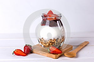 Jar of granola with yogurt, strawberry jam and fresh strawberries on a white wooden background. Healthy food