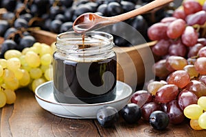 Jar of grape molasses, grape syrup. Sweetener, cough medicine. Black, green and purple grapes on table