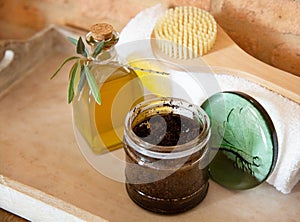 A jar of handmade coffee scrub, body brush with bottle of olive oil and white towel are on wooden background.