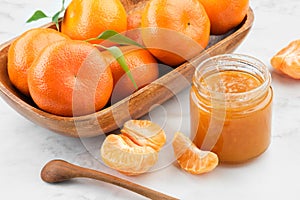 Jar of healthy tangerine jam and wooden bowl of mandarin oranges fruits on kitchen table