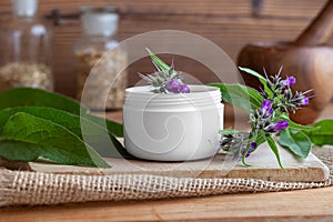 A jar of homemade comfrey root ointment with fresh blooming comfrey plant