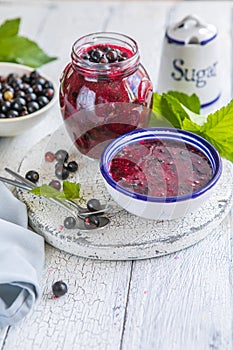 Jar of homemade fresh currant jam with shugar. Fresh berries black currant on white wooden background