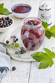 Jar of homemade fresh currant jam with shugar. Fresh berries black currant on white wooden background