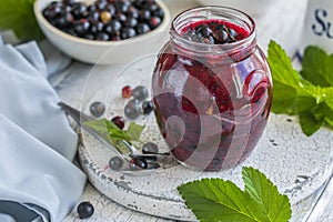 Jar of homemade fresh currant jam with shugar. Fresh berries black currant on white wooden background