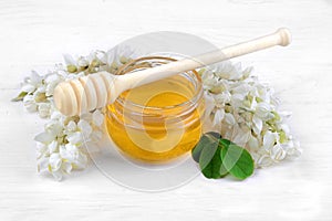 Jar with honey and acacia flowers on a white wooden background