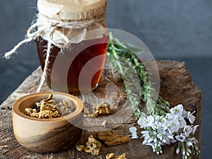 Jar of honey, flowers and wooden bowl of propolis granules on piece of wood.