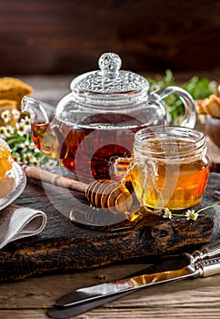 Jar of honey with honey dipper and teapot with hot tea close-up