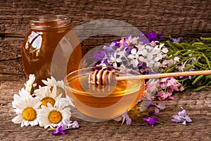 Jar of honey with wildflowers and chamomile on old wooden background