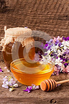 Jar of honey with wildflowers on old wooden background