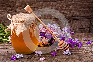 Jar of honey with wildflowers on old wooden background