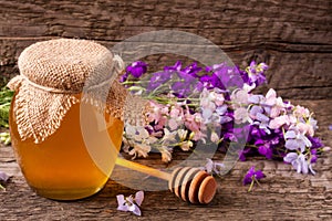 Jar of honey with wildflowers on old wooden background