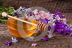 Jar of honey with wildflowers on old wooden background