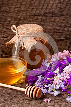 Jar of honey with wildflowers on old wooden background