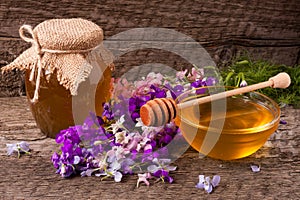 Jar of honey with wildflowers on old wooden background