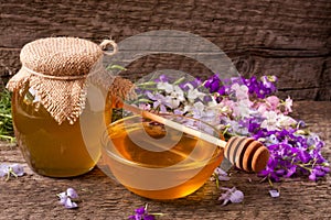 Jar of honey with wildflowers on old wooden background