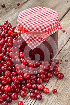 Jar of jam and fresh red cranberries on wooden table.