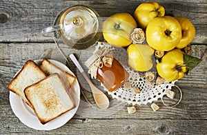 jar of jam with sandwich and quinces with leaves on wooden rustic background