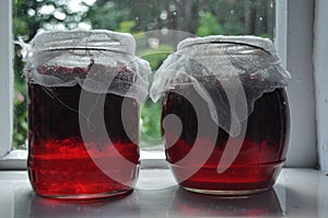 Jar, jars of jam with red currants standing on the windowsill in the farmhouse.