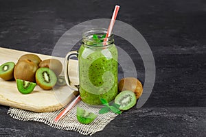 A jar of kiwi juice on a black table background. Fresh kiwi fruits on a cutting desk. Healthy green juice. Copy space.