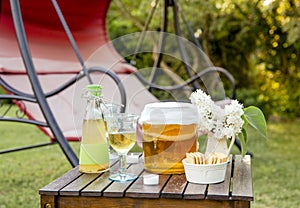 Jar with kombucha drink and tea mushroom in it and served in goblet glass outdoors in sunny summer evening.