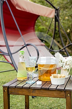 Jar with kombucha drink and tea mushroom in it and served in goblet glass outdoors in sunny summer evening, garden swing.