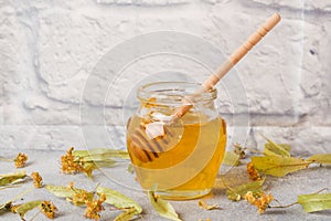 Jar of liquid honey from Linden flowers and a stick on grey concrete background. Copy space