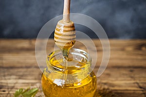 A jar of liquid honey from Linden flowers and a stick with honey on a dark background. Copy space