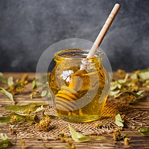 A jar of liquid honey from Linden flowers and a stick with honey on a dark background. Copy space