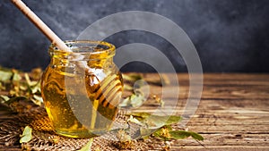 A jar of liquid honey from Linden flowers and a stick with honey on a dark background. Copy space
