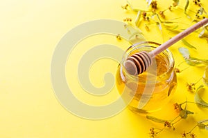 A jar of liquid honey from Linden flowers and a stick with honey on yellow background. Copy space