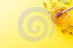 A jar of liquid honey from Linden flowers and a stick with honey on yellow background. Copy space