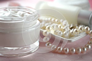 A jar of luxury beauty face cream and serum bottle with pearls on pink color background with copy space.