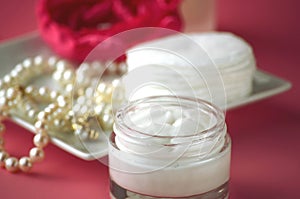 A jar of luxury beauty face cream and serum bottle with pearls on pink color background with copy space.