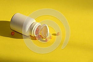A jar of medicine on a yellow background. An open white bottle, yellow pills spilled out.