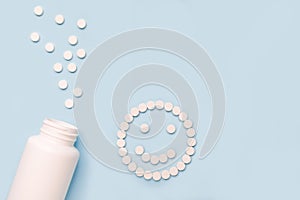 A jar with medicines and happy face made of pills on blue background. The concept of antidepressants