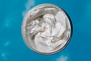 Jar with moisturizing cream on the reflections of blue skies