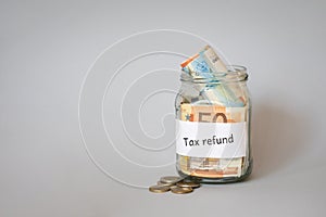 jar of money with inscription tax refund on gray background