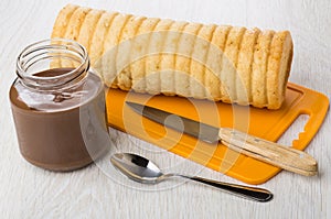 Jar with nut-chocolate paste, bread, knife on cutting board