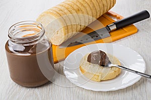 Jar with nut-chocolate paste, bread, knife, teaspoon with paste