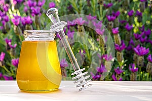 Jar of organic floral honey with a drizzle against lavender background . Outdoor