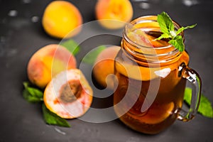 Jar of peach iced tea with fresh peaches on the rustic background